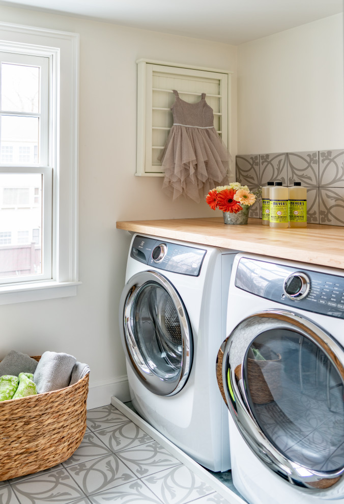 Photo of a small transitional galley dedicated laundry room in Boston with wood benchtops, white walls, porcelain floors, a side-by-side washer and dryer and grey floor.