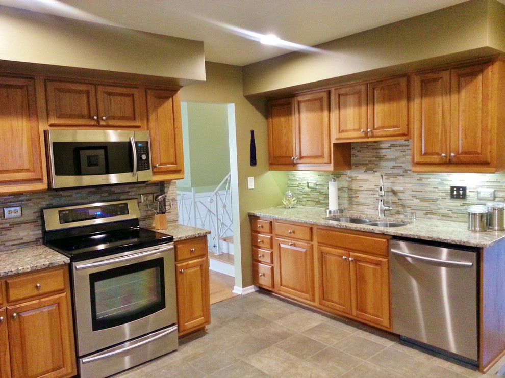 Example of a mid-sized transitional u-shaped ceramic tile enclosed kitchen design in Chicago with an undermount sink, raised-panel cabinets, medium tone wood cabinets, granite countertops, beige backsplash, glass sheet backsplash, stainless steel appliances and no island