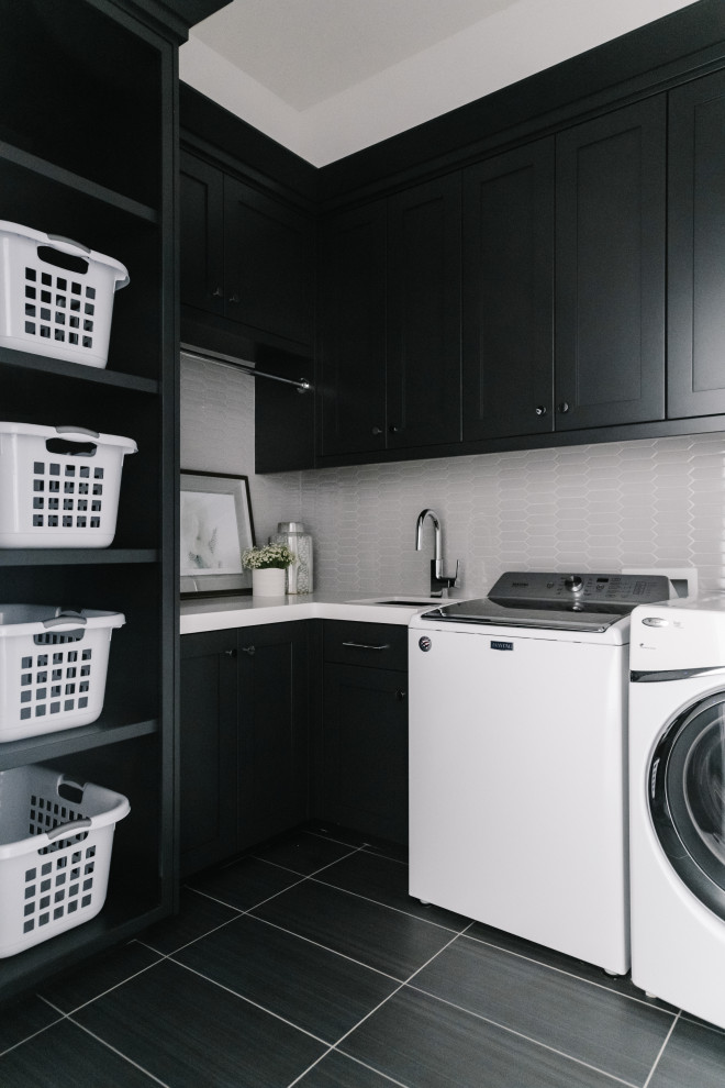 ソルトレイクシティにあるトランジショナルスタイルのおしゃれな洗濯室 (L型、アンダーカウンターシンク、シェーカースタイル扉のキャビネット、黒いキャビネット、グレーのキッチンパネル、モザイクタイルのキッチンパネル、黒い壁、左右配置の洗濯機・乾燥機、黒い床、白いキッチンカウンター) の写真