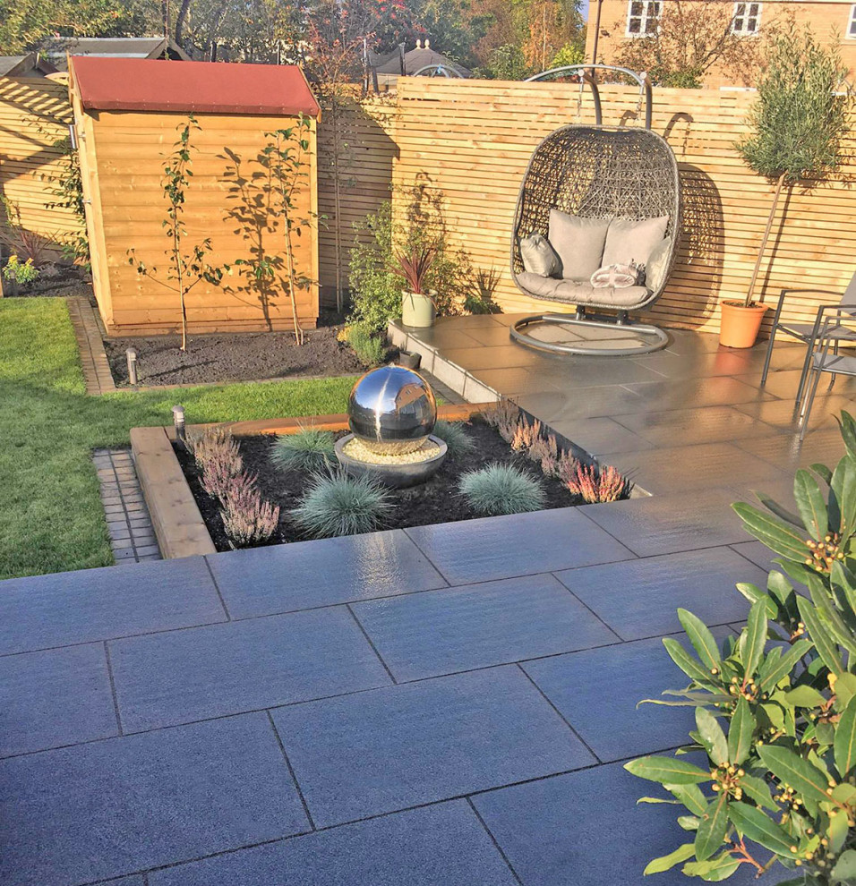 This is an example of a medium sized contemporary back patio in Hertfordshire with natural stone paving.