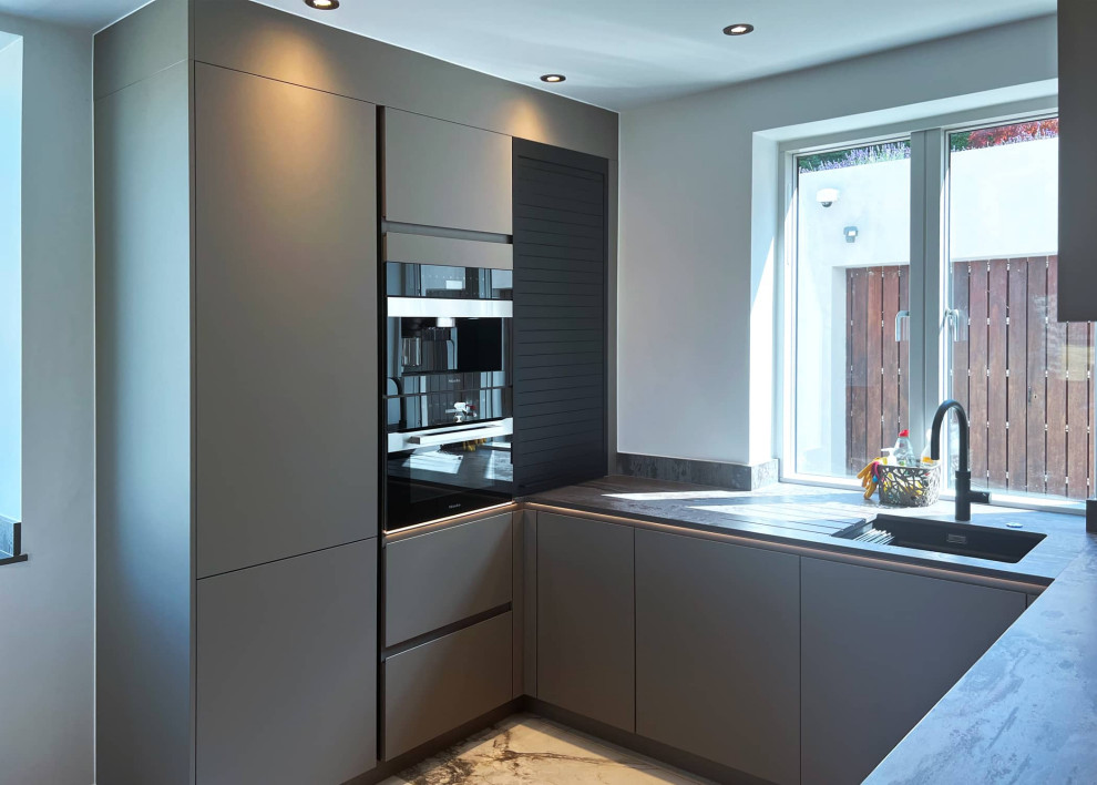 Свежая идея для дизайна: п-образная кухня-гостиная среднего размера в стиле модернизм с плоскими фасадами, серыми фасадами, черной техникой, островом и коричневой столешницей - отличное фото интерьера
