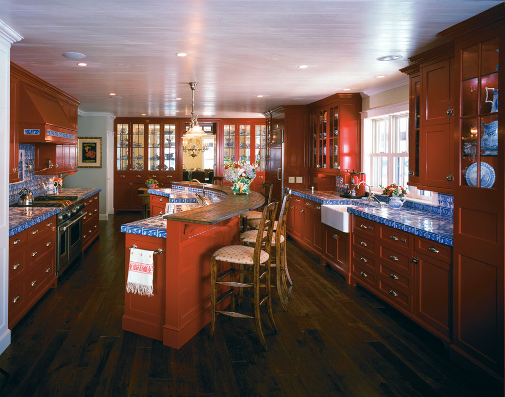 Photo of a large traditional eat-in kitchen in Boston with recessed-panel cabinets, a farmhouse sink, tile benchtops, red cabinets, blue splashback, ceramic splashback, panelled appliances, dark hardwood floors and with island.