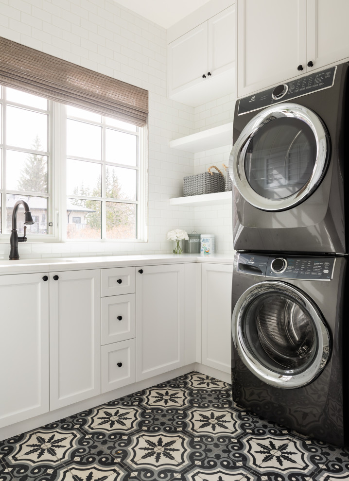 This is an example of a mid-sized transitional u-shaped dedicated laundry room in Calgary with an undermount sink, shaker cabinets, white cabinets, quartzite benchtops, white splashback, subway tile splashback, white walls, ceramic floors, a stacked washer and dryer and white benchtop.