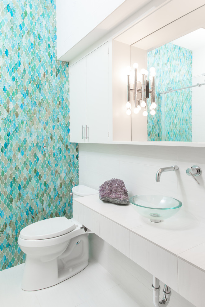 This is an example of a small midcentury kids bathroom in New Orleans with flat-panel cabinets, white cabinets, an alcove tub, a shower/bathtub combo, a two-piece toilet, blue tile, glass tile, white walls, porcelain floors, a vessel sink, tile benchtops, white floor, a sliding shower screen, white benchtops, a niche, a single vanity, a floating vanity and decorative wall panelling.