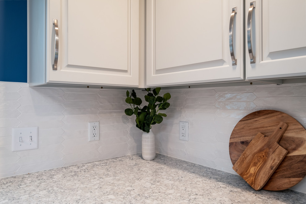 Mid-sized transitional l-shaped light wood floor eat-in kitchen photo in Boston with a single-bowl sink, raised-panel cabinets, gray cabinets, quartz countertops, white backsplash, ceramic backsplash, stainless steel appliances, an island and white countertops