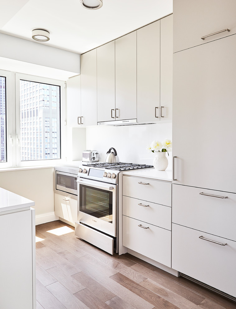 Inspiration for a small contemporary u-shaped separate kitchen in New York with flat-panel cabinets, white cabinets, stainless steel appliances, light hardwood floors, beige floor, an undermount sink, solid surface benchtops, white splashback, stone slab splashback and no island.