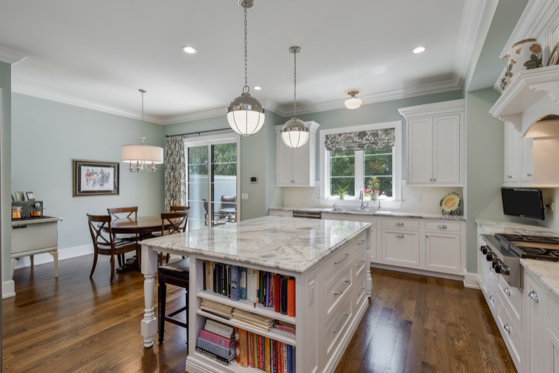 This is an example of a mid-sized traditional u-shaped separate kitchen in Chicago with an undermount sink, beaded inset cabinets, white cabinets, marble benchtops, white splashback, marble splashback, stainless steel appliances, medium hardwood floors, with island and brown floor.
