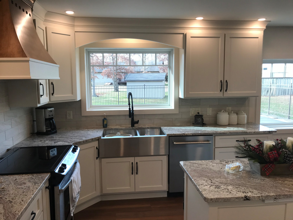 Example of a mid-sized minimalist u-shaped vinyl floor and brown floor eat-in kitchen design with a farmhouse sink, recessed-panel cabinets, white cabinets, granite countertops, gray backsplash, porcelain backsplash, stainless steel appliances, an island and gray countertops