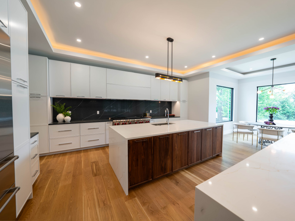 Example of a transitional medium tone wood floor and tray ceiling kitchen design in Boston with two islands, an undermount sink, shaker cabinets, quartz countertops, black backsplash, quartz backsplash, stainless steel appliances and white countertops