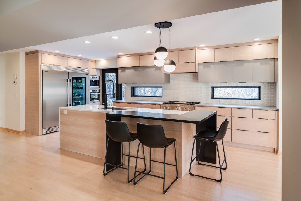 This is an example of a contemporary l-shaped kitchen in Minneapolis with an undermount sink, flat-panel cabinets, light wood cabinets, stainless steel appliances, light hardwood floors, with island, beige floor and grey benchtop.