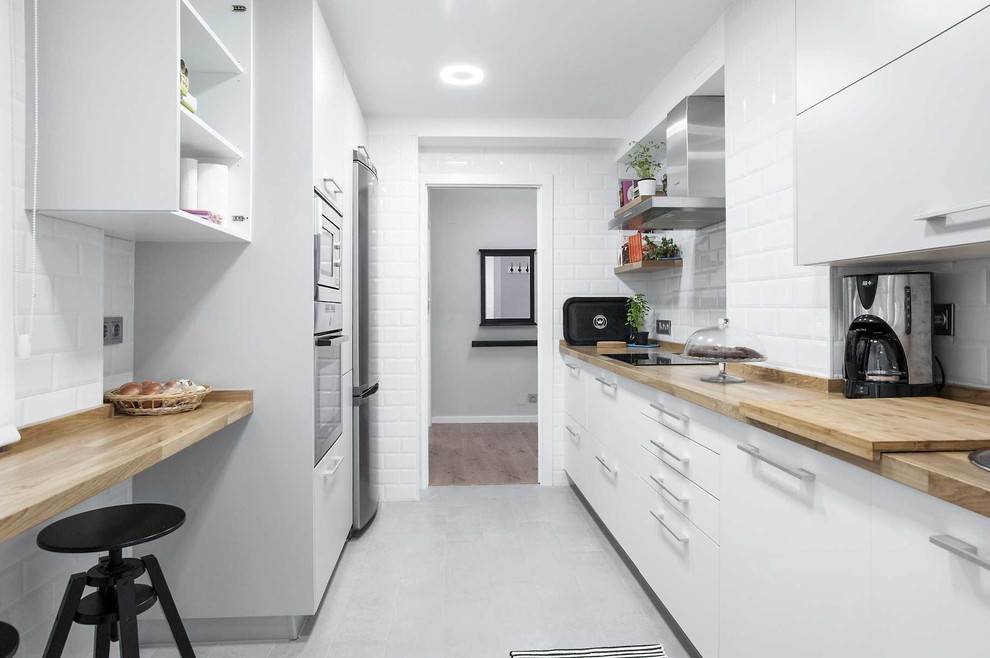 Inspiration for a mid-sized scandinavian galley separate kitchen in Other with flat-panel cabinets, white cabinets, wood benchtops, white splashback, subway tile splashback, stainless steel appliances, ceramic floors and no island.