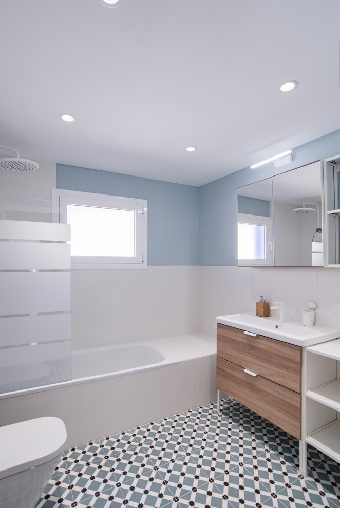 Réalisation d'une grande salle de bain principale et grise et blanche minimaliste avec un placard à porte plane, des portes de placard blanches, une baignoire posée, un combiné douche/baignoire, WC à poser, un carrelage blanc, des carreaux de céramique, un mur bleu, un sol en carrelage de céramique, un lavabo posé, un plan de toilette en surface solide, un sol multicolore, une cabine de douche à porte battante, un plan de toilette blanc, une fenêtre, meuble simple vasque et meuble-lavabo sur pied.