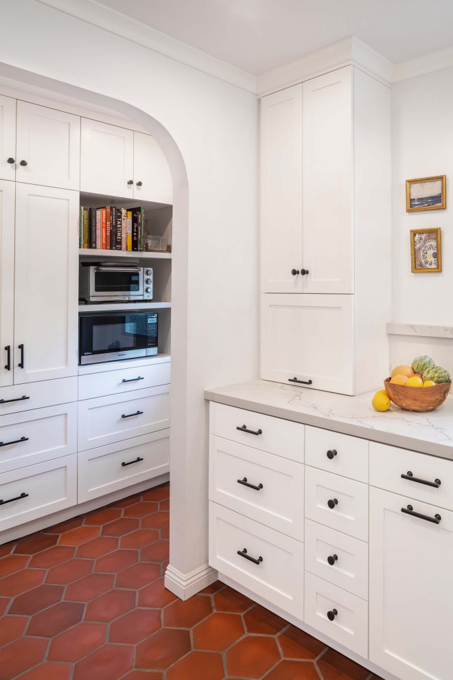 Exempel på ett mellanstort medelhavsstil vit vitt kök, med en rustik diskho, skåp i shakerstil, vita skåp, bänkskiva i kvarts, vitt stänkskydd, rostfria vitvaror, klinkergolv i terrakotta, en halv köksö och rött golv