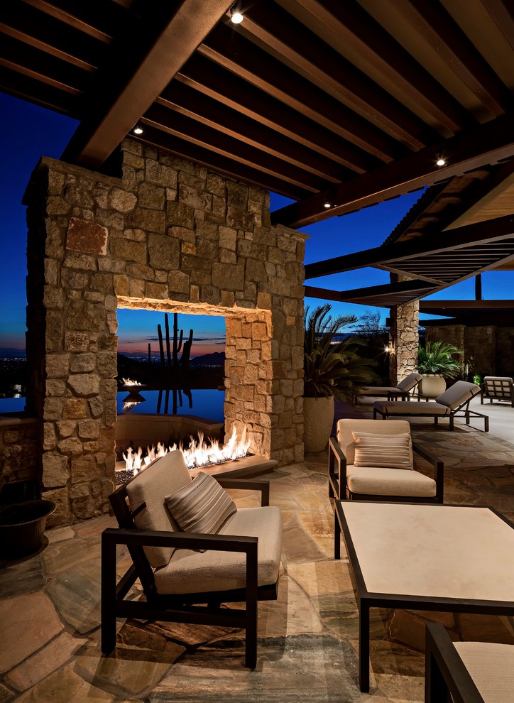 Photo of an expansive contemporary backyard patio in Phoenix with a fire feature, natural stone pavers and a roof extension.