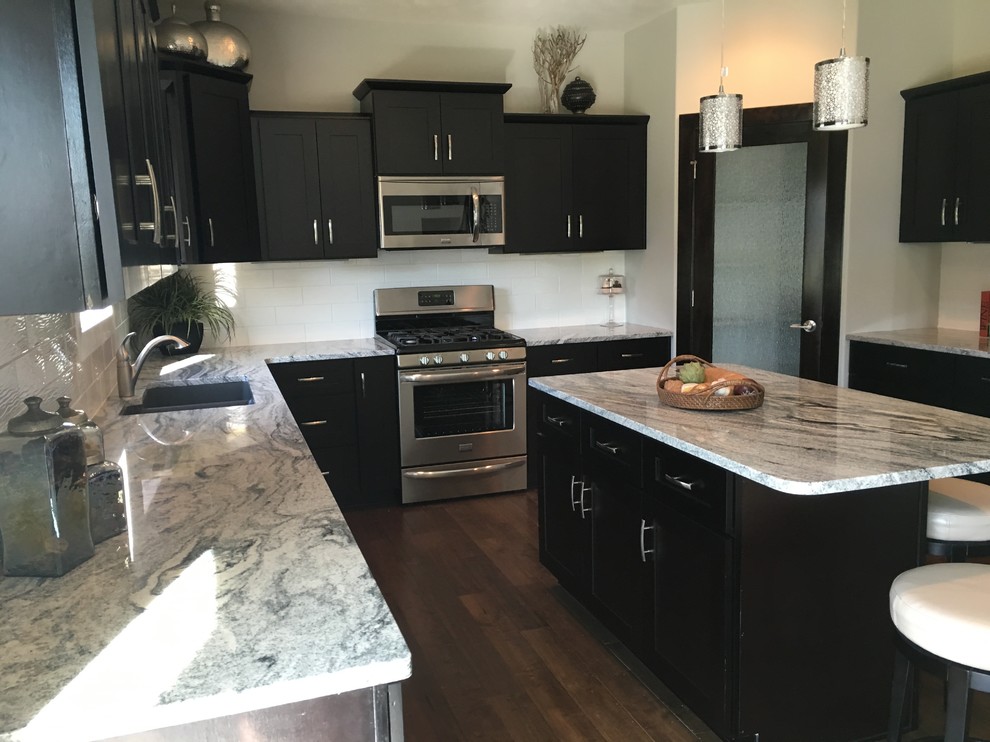 Mid-sized contemporary u-shaped eat-in kitchen in Omaha with a farmhouse sink, shaker cabinets, dark wood cabinets, granite benchtops, white splashback, ceramic splashback, stainless steel appliances, dark hardwood floors and with island.