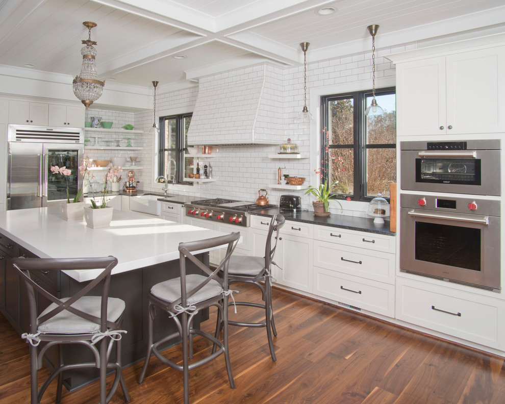 Large transitional u-shaped medium tone wood floor and brown floor eat-in kitchen photo with white cabinets, soapstone countertops, white backsplash, ceramic backsplash, stainless steel appliances, an island, a farmhouse sink and shaker cabinets
