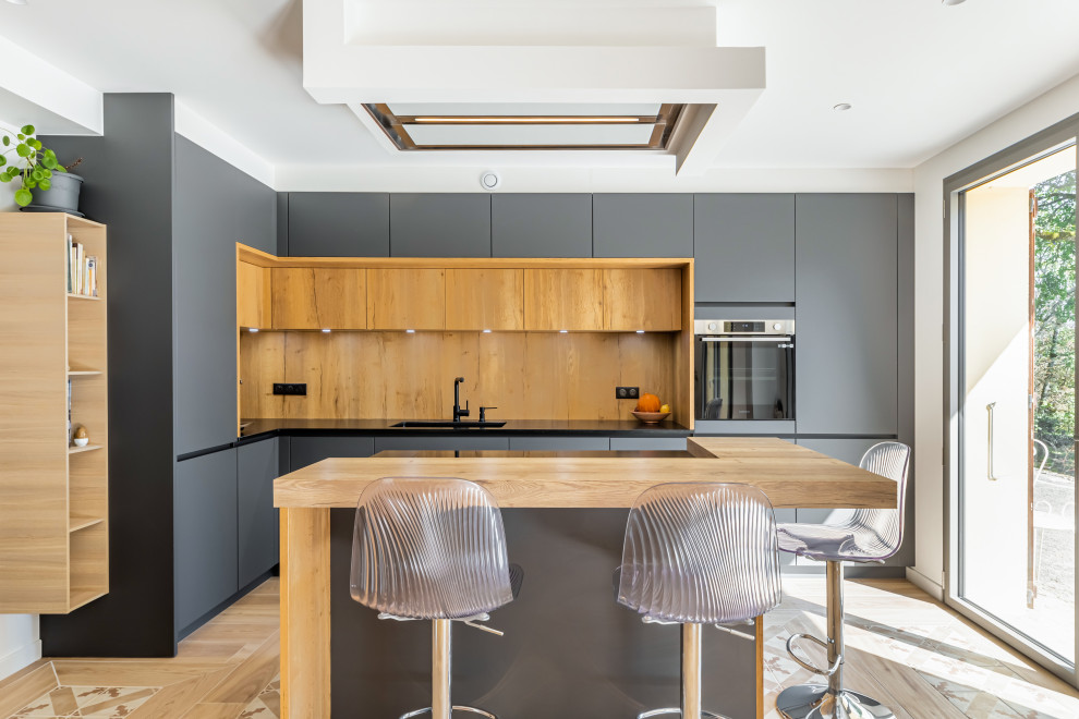 Inspiration for a medium sized contemporary l-shaped open plan kitchen in Grenoble with a submerged sink, grey cabinets, granite worktops, wood splashback, black appliances, ceramic flooring, an island, beige floors and black worktops.