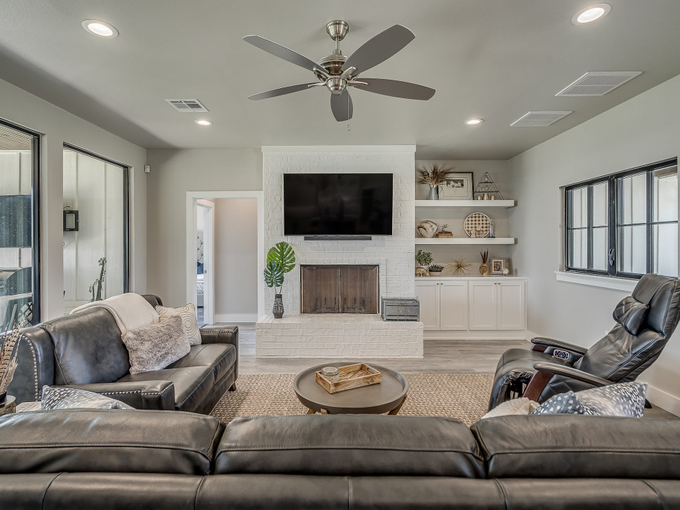 Inspiration for a mid-sized country open concept living room with white walls, ceramic floors, a brick fireplace surround, a wall-mounted tv and grey floor.