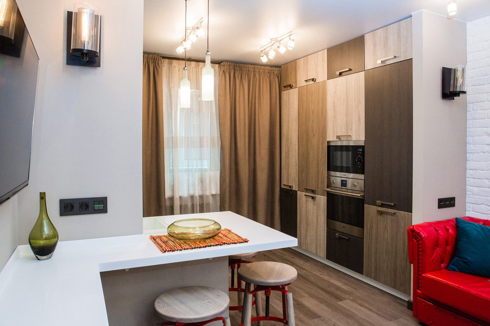 Inspiration for a small modern galley eat-in kitchen in Novosibirsk with a drop-in sink, flat-panel cabinets, light wood cabinets, solid surface benchtops, glass sheet splashback, black appliances, a peninsula and white benchtop.