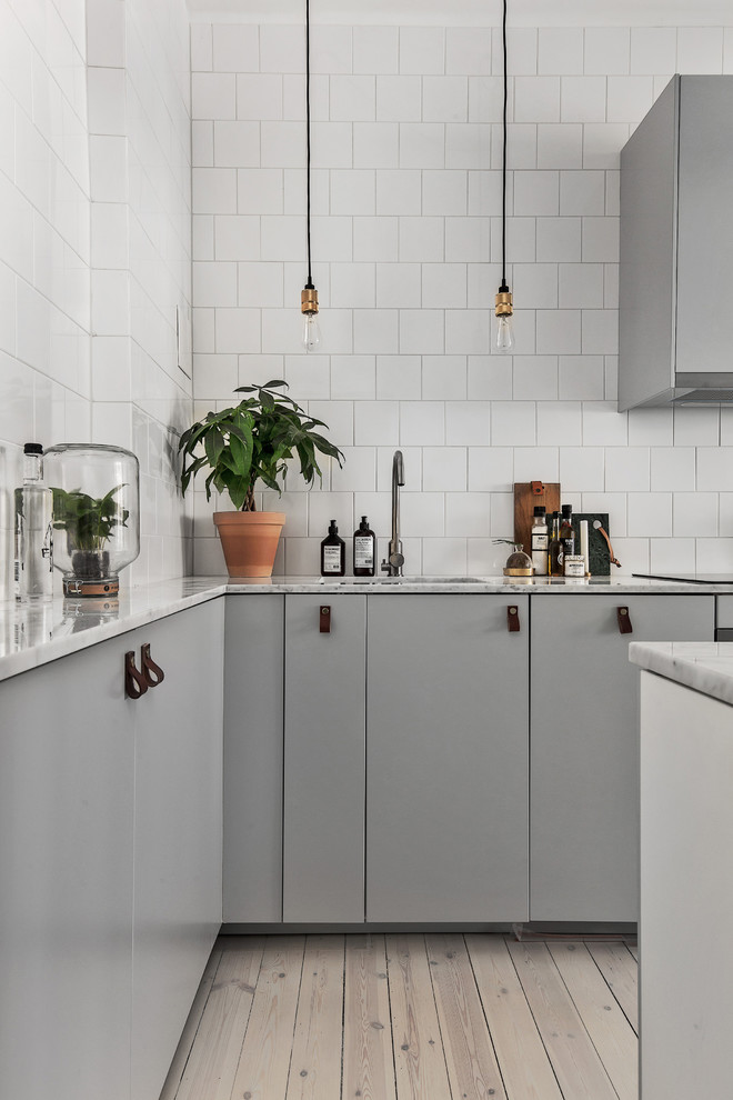 Scandinavian l-shaped kitchen in Stockholm with a single-bowl sink, flat-panel cabinets, grey cabinets, marble benchtops and light hardwood floors.