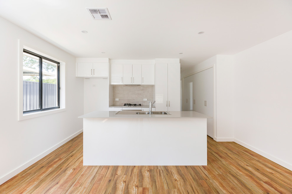 Inspiration for a small traditional galley eat-in kitchen in Canberra - Queanbeyan with a double-bowl sink, flat-panel cabinets, white cabinets, quartz benchtops, grey splashback, porcelain splashback, stainless steel appliances, vinyl floors, with island, brown floor and grey benchtop.