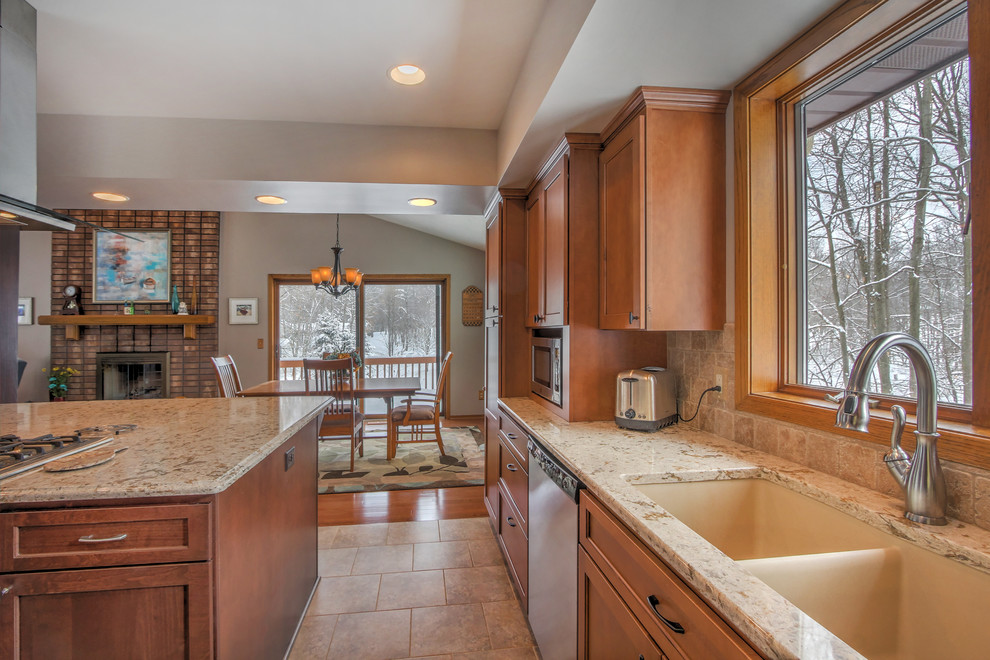 Mid-sized traditional u-shaped open plan kitchen in Grand Rapids with flat-panel cabinets, medium wood cabinets, granite benchtops, brown splashback, ceramic splashback, stainless steel appliances, ceramic floors and a double-bowl sink.