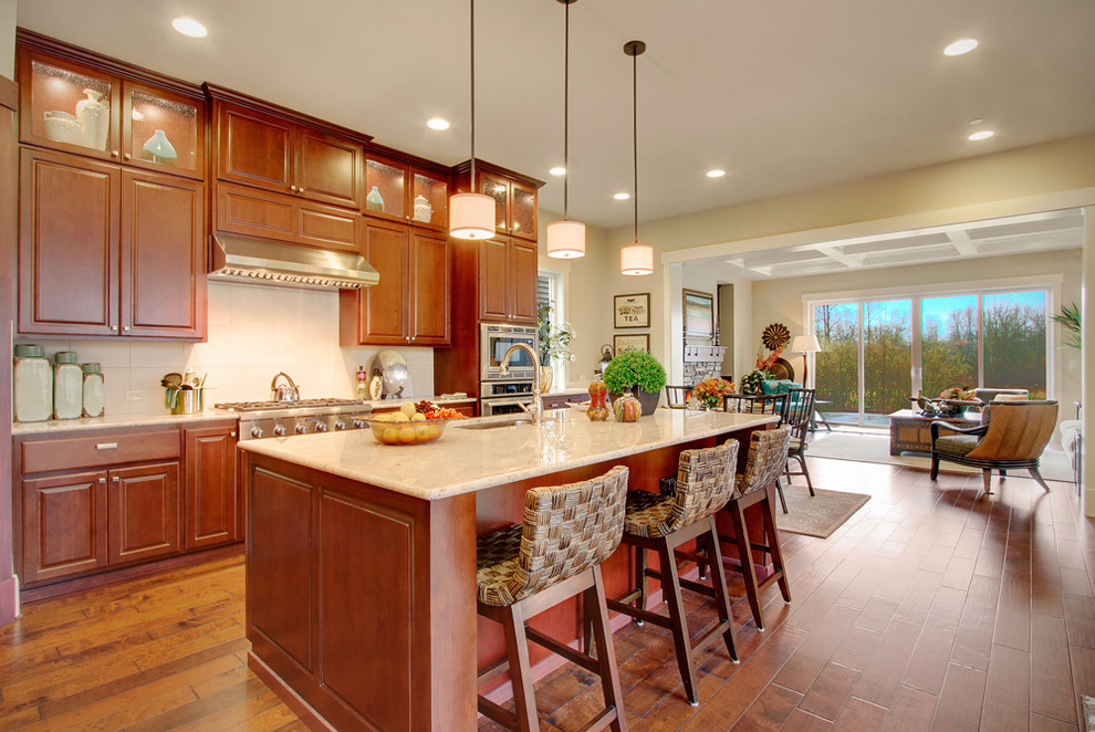Large traditional l-shaped eat-in kitchen in Seattle with an undermount sink, raised-panel cabinets, medium wood cabinets, granite benchtops, white splashback, ceramic splashback, stainless steel appliances, medium hardwood floors, with island, brown floor and beige benchtop.