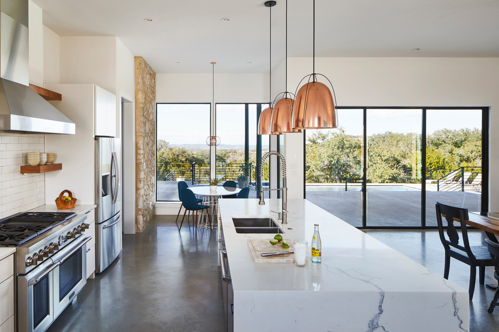 This is an example of a large modern single-wall eat-in kitchen in Austin with an undermount sink, flat-panel cabinets, white cabinets, quartz benchtops, white splashback, ceramic splashback, stainless steel appliances, concrete floors, with island, grey floor and white benchtop.