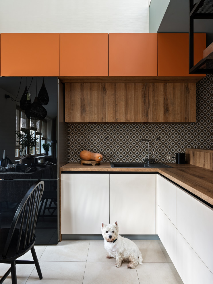 Foto på ett stort funkis kök, med en nedsänkt diskho, släta luckor, orange skåp, stänkskydd i porslinskakel, svarta vitvaror, klinkergolv i porslin och beiget golv