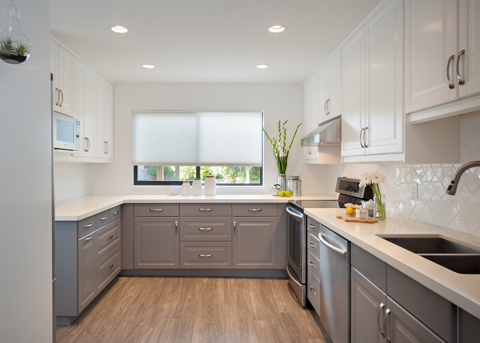 Photo of a traditional u-shaped separate kitchen in Vancouver with a double-bowl sink, quartz benchtops, white splashback, subway tile splashback, stainless steel appliances and no island.
