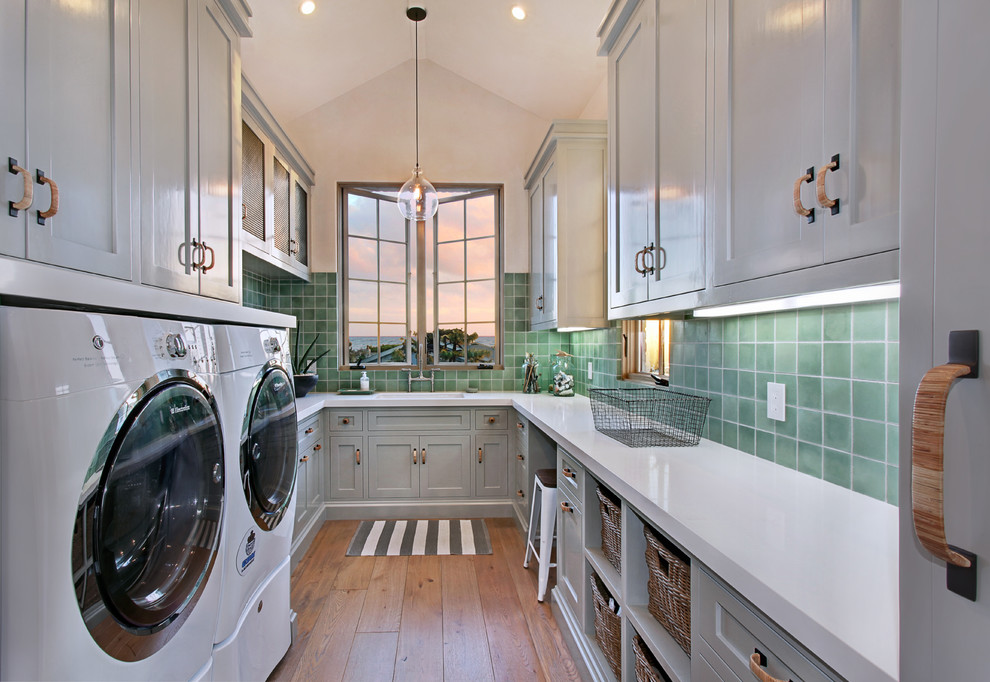 Design ideas for a traditional u-shaped laundry room in Los Angeles with an undermount sink, shaker cabinets, grey cabinets, medium hardwood floors, a side-by-side washer and dryer, brown floor and white benchtop.