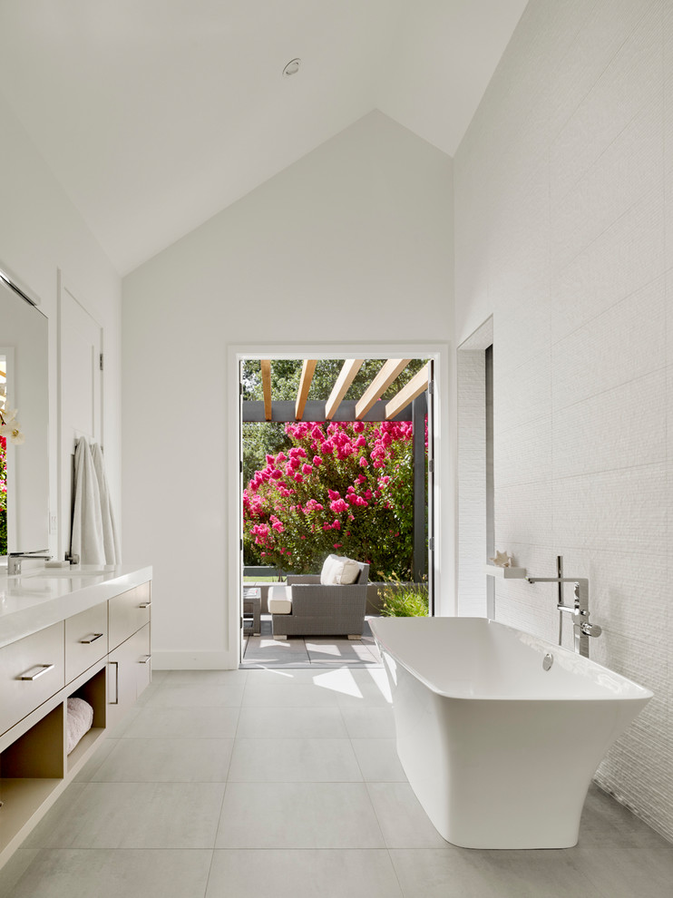 This is an example of a contemporary master bathroom in San Francisco with a freestanding tub, white tile, white walls, flat-panel cabinets, light wood cabinets, an undermount sink, white floor and white benchtops.