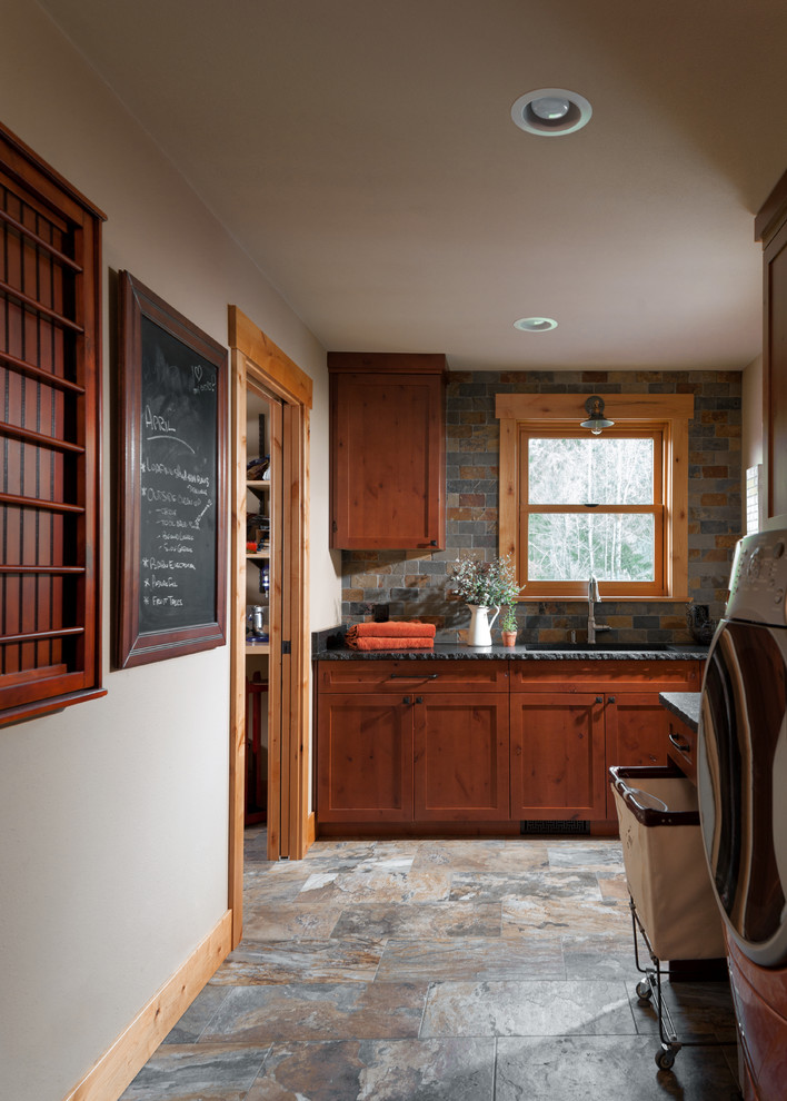 Inspiration for a mid-sized country l-shaped utility room in Seattle with an undermount sink, shaker cabinets, medium wood cabinets, granite benchtops, beige walls, porcelain floors, a side-by-side washer and dryer and grey floor.