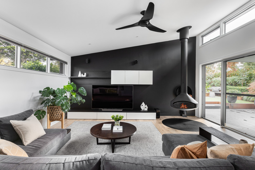 Inspiration for a large contemporary open concept living room in Melbourne with black walls, light hardwood floors and a hanging fireplace.
