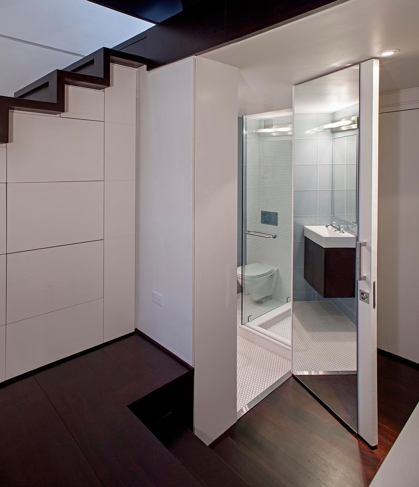 Photo of a small modern master bathroom in New York with a wall-mount sink, a corner shower, glass tile, white walls, ceramic floors, flat-panel cabinets, white cabinets, a wall-mount toilet and white tile.