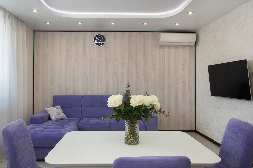 Идея дизайна: объединенная гостиная комната в современном стиле с белыми стенами, полом из ламината, телевизором на стене, бежевым полом, многоуровневым потолком и панелями на части стены