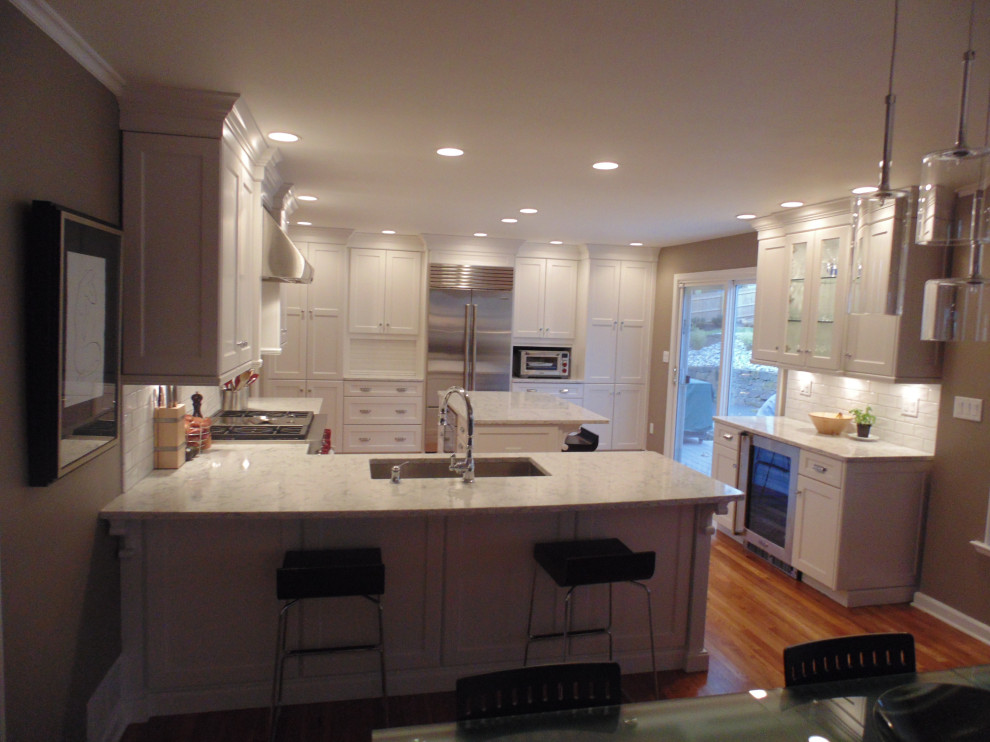Inspiration for a large transitional u-shaped medium tone wood floor and brown floor eat-in kitchen remodel with an undermount sink, recessed-panel cabinets, white cabinets, quartz countertops, white backsplash, subway tile backsplash, stainless steel appliances, an island and white countertops