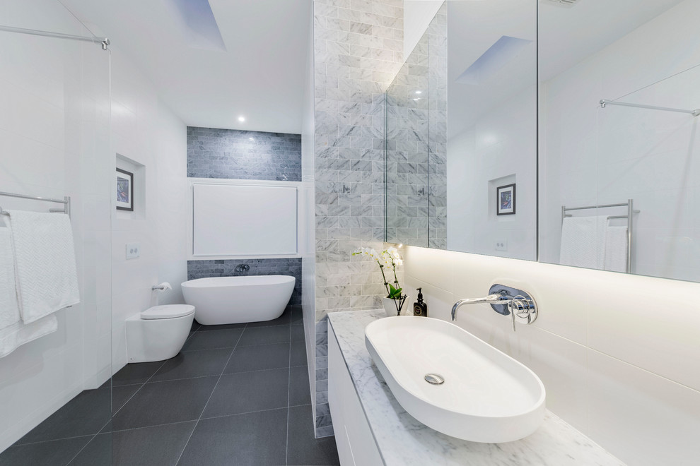 Photo of a mid-sized contemporary bathroom in Melbourne with white cabinets, a freestanding tub, a wall-mount toilet, ceramic tile, white walls, ceramic floors and a vessel sink.