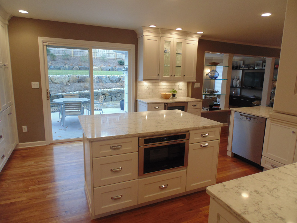Inspiration for a large transitional u-shaped medium tone wood floor and brown floor eat-in kitchen remodel with an undermount sink, recessed-panel cabinets, white cabinets, quartz countertops, white backsplash, subway tile backsplash, stainless steel appliances, an island and white countertops