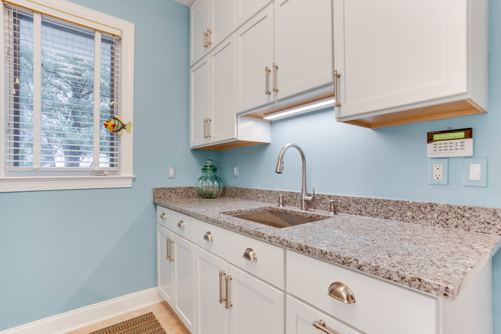 Inspiration for a mid-sized transitional galley dedicated laundry room in Baltimore with an undermount sink, shaker cabinets, white cabinets, granite benchtops, blue walls and a stacked washer and dryer.