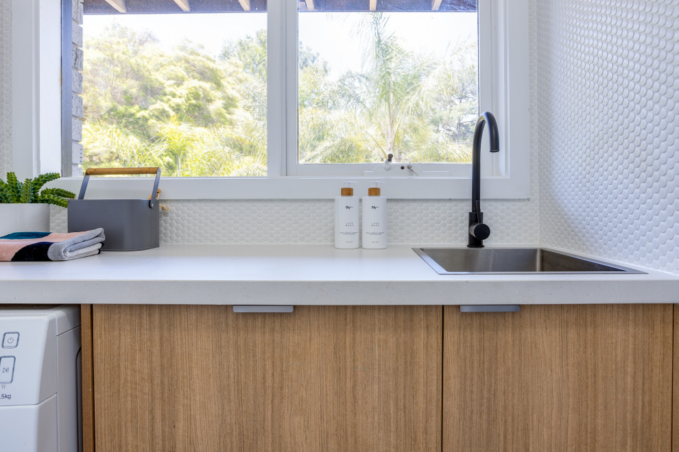 This is an example of a small scandinavian galley dedicated laundry room in Melbourne with a drop-in sink, open cabinets, light wood cabinets, quartz benchtops, white walls, medium hardwood floors, a side-by-side washer and dryer and white benchtop.