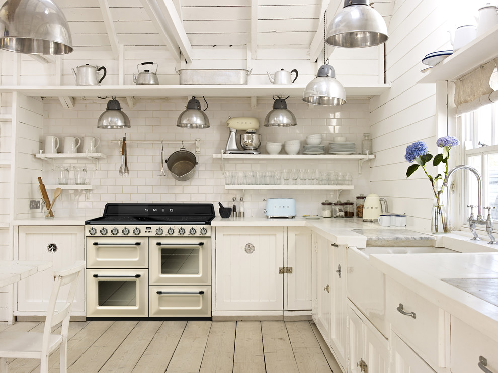 Bild på ett shabby chic-inspirerat vit vitt l-kök, med en rustik diskho, skåp i shakerstil, vita skåp, vitt stänkskydd, stänkskydd i tunnelbanekakel, vita vitvaror, ljust trägolv, en köksö och beiget golv