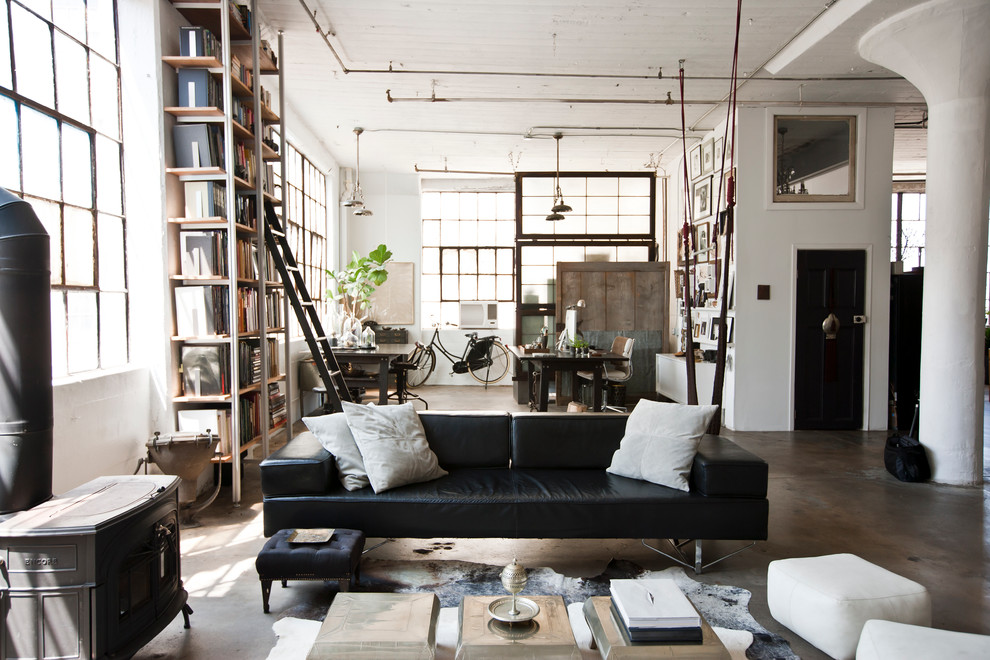 This is an example of an industrial living room in New York with concrete floors, a wood stove and grey floor.