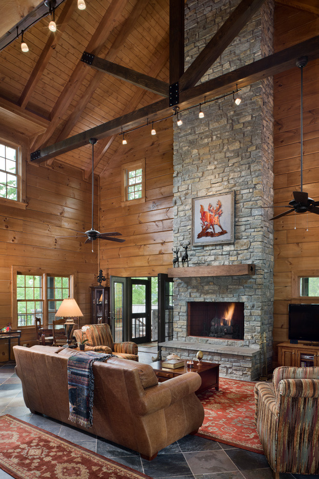 Large country living room in Nashville with brown walls, slate floors, a stone fireplace surround and a corner tv.