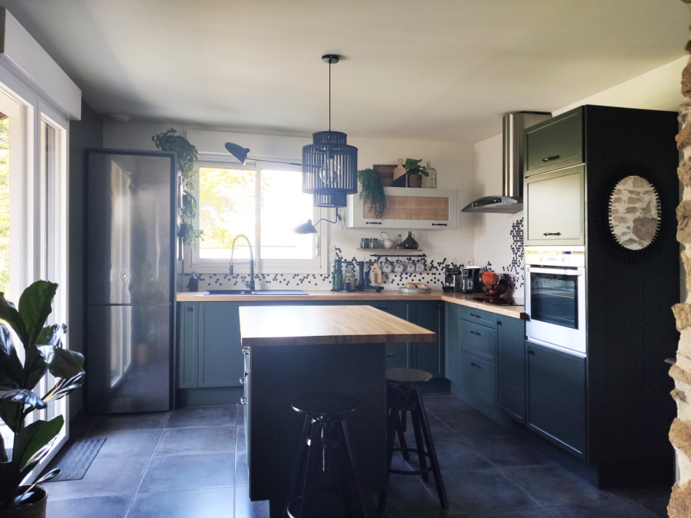 Inredning av ett industriellt mellanstort kök, med en enkel diskho, gröna skåp, träbänkskiva, vitt stänkskydd, stänkskydd i keramik, integrerade vitvaror, en köksö och grått golv