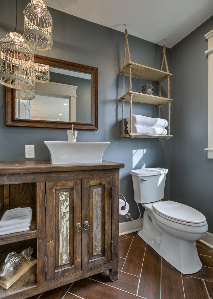 Inspiration for a country powder room in Kansas City with raised-panel cabinets, medium wood cabinets, a two-piece toilet, grey walls, a vessel sink, wood benchtops, brown floor and brown benchtops.