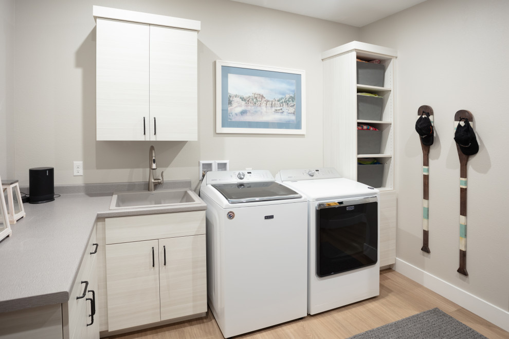 This is an example of a beach style l-shaped dedicated laundry room in Other with a drop-in sink, flat-panel cabinets, white cabinets, laminate benchtops and grey benchtop.