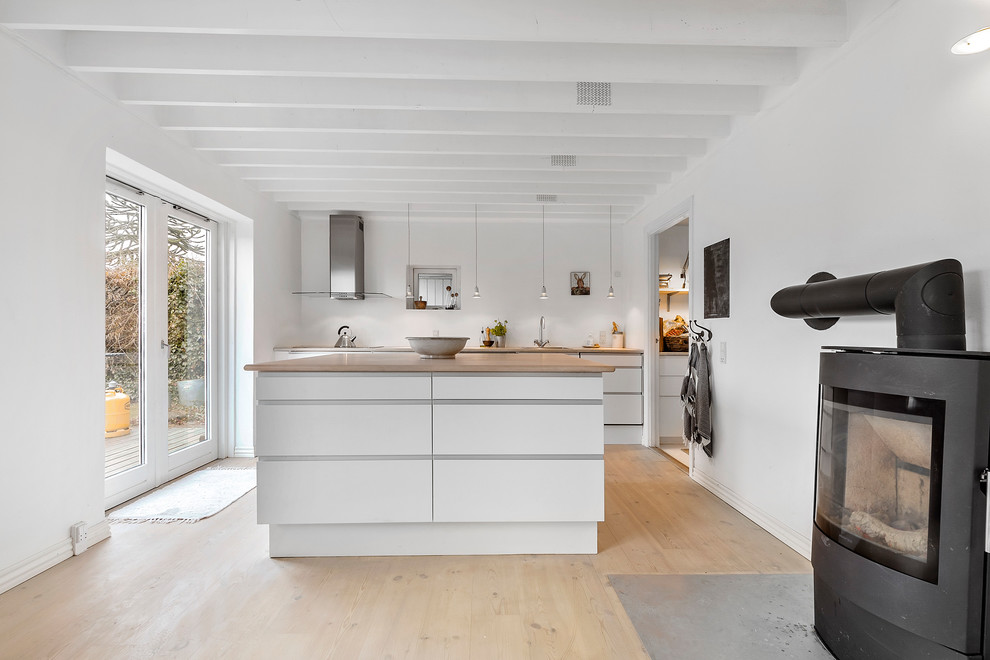 This is an example of a mid-sized scandinavian galley kitchen in Copenhagen with flat-panel cabinets, white cabinets, wood benchtops, white splashback, light hardwood floors, with island, beige floor, beige benchtop and panelled appliances.