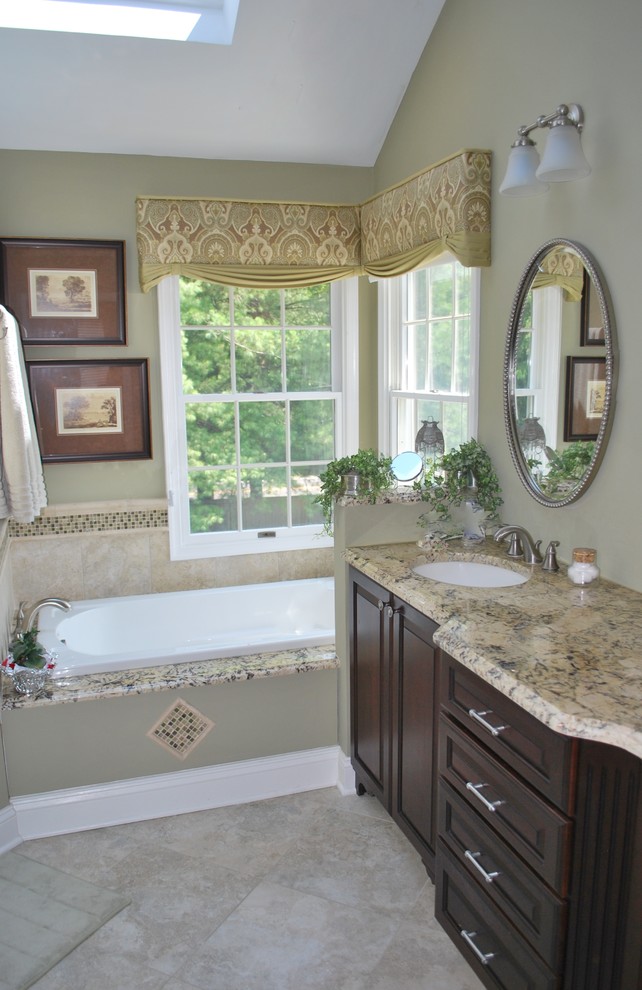 Photo of a mid-sized traditional master bathroom in New York with raised-panel cabinets, dark wood cabinets, a drop-in tub, a one-piece toilet, beige walls, travertine floors, an undermount sink and granite benchtops.
