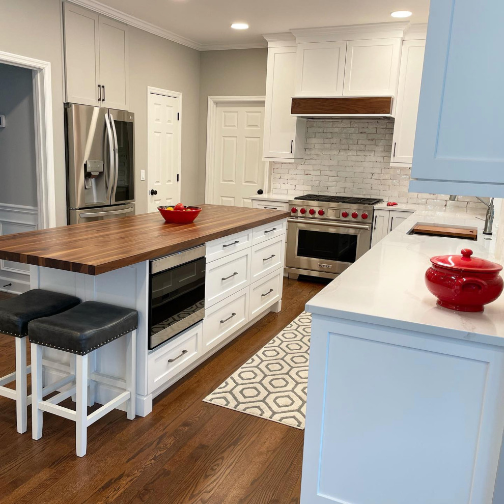 Medium tone wood floor and brown floor kitchen photo in Atlanta with an undermount sink, recessed-panel cabinets, white cabinets, white backsplash, stainless steel appliances, an island and white countertops